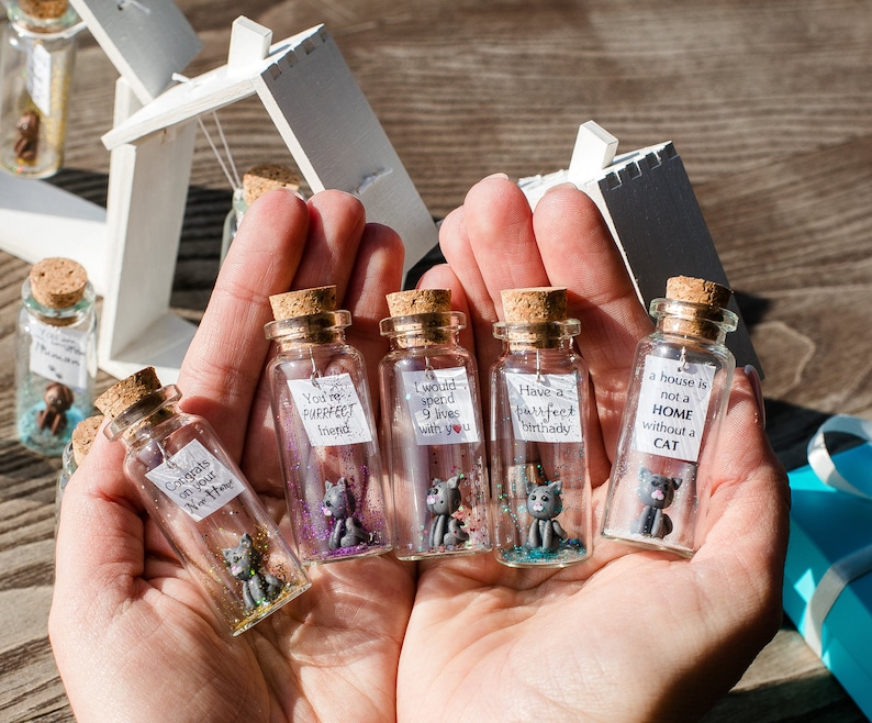 a person holding four miniature bottles with miniature cats in them