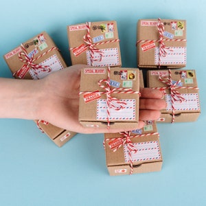 K&ouml;nnte beinhalten: Sechs kleine braune Kartons, die mit rotem und wei&szlig;em Garn gebunden sind. Jede Schachtel hat ein "Special Delivery" und "Fragile" Etikett und ist mit Vintage-Briefmarken verziert.