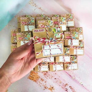 May include: A collection of small square cardboard gift boxes wrapped in red and white baker's twine. Each box features printed postage stamps, a 'SPECIAL DELIVERY' label, and a 'FROM' and 'TO' address field with red and blue striped borders.