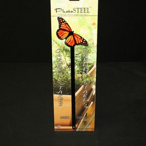 May include: A double-sided garden stake featuring a monarch butterfly design. The butterfly has orange and black wings. The stake is black and has the words "Garden Stakes" printed on the packaging. The packaging also includes the text "PhotoSteel" and "Making memories permanent."