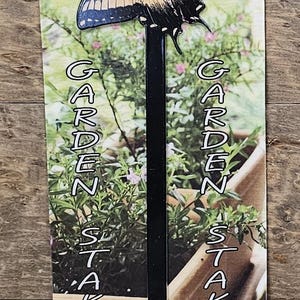 May include: A PhotoSTEEL garden stake featuring a yellow and black butterfly design on a display card. The card includes the text PhotoSTEEL Making memories permanent, GARDEN STAKES, and DOUBLE SIDED. The stake is a long, thin, black metal rod.