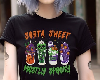 May include: Black t-shirt with a Halloween-themed design. The text "Sorta Sweet Mostly Spooky" is printed on the shirt. The design features four cartoon milkshakes with spooky Halloween-themed toppings.