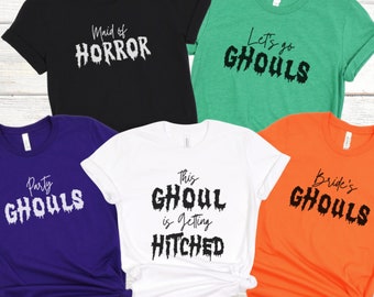 May include: Five t-shirts with different Halloween-themed designs. The shirts are black, green, purple, white, and orange. The text on the shirts reads "Maid of Horror", "Let's go Ghouls", "Party Ghouls", "This Ghoul is getting Hitched", and "Bride's Ghouls".