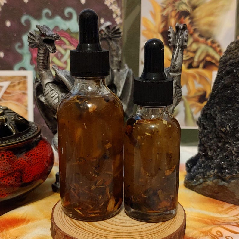 Peut inclure: Deux flacons en verre avec des compte-gouttes remplis d'un liquide brun et d'herbes. Les flacons sont pos&eacute;s sur une surface en bois.