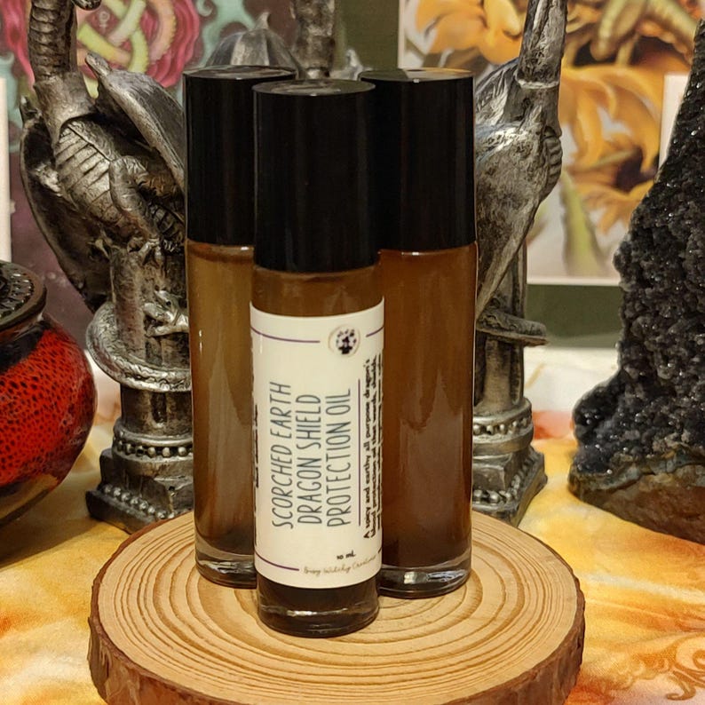 Peut inclure: Trois flacons roulants en verre brun avec des bouchons noirs et des &eacute;tiquettes blanches. L'&eacute;tiquette du flacon du milieu indique "Scorched Earth Dragon Shield Protection Oil".