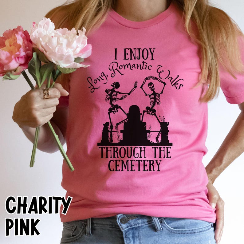 May include: Pink t-shirt with the text "I Enjoy Long Romantic Walks Through The Cemetery" and a graphic of dancing skeletons. The shirt also has the words "Charity Pink" printed on it.