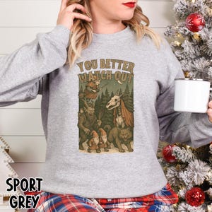 May include: Sport grey sweatshirt with a graphic that reads "YOU BETTER WATCH OUT". The graphic features a witch on a broom, gnomes, a wolf, and a horse skull in a forest setting.