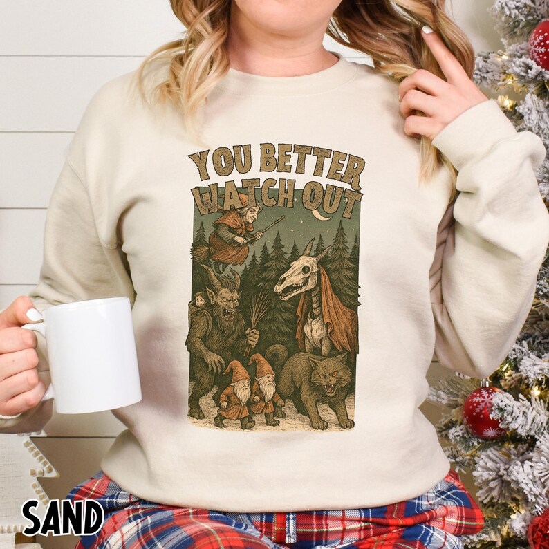 May include: Sand-colored sweatshirt with the text "YOU BETTER WATCH OUT" above a graphic of forest creatures. The graphic includes a witch on a broom, a horse skull, gnomes, a wolf, and a goblin.