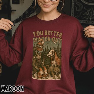 May include: Maroon sweatshirt with the text "YOU BETTER WATCH OUT" above a graphic of fantasy creatures in a forest scene. The graphic includes a witch, gnomes, a skeletal horse, a cat, and a goblin. The word "MAROON" is printed at the bottom.