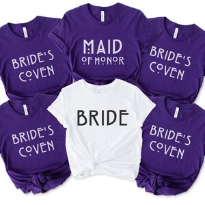May include: Five purple t-shirts with white text that reads "Bride's Coven" and one white t-shirt with black text that reads "Bride". One purple t-shirt has white text that reads "Maid of Honor".
