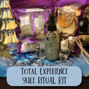 May include: A Yule Ritual Kit with various components, including glass bottles, spray bottles, and pouches. The kit features a clear glass bottle with a dropper, a small decorative bottle, and a silver pendant. The text "TOTAL EXPERIENCE YULE RITUAL KIT" is displayed.