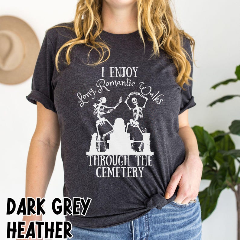 May include: Dark grey heather t-shirt with white text and a skeleton graphic. The text reads "I Enjoy Long Romantic Walks Through The Cemetery". The shirt has short sleeves and a crew neck.