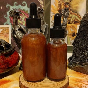 Peut inclure: Deux flacons en verre ambr&eacute; avec des compte-gouttes, remplis d'un liquide orange chatoyant. Les flacons sont pos&eacute;s sur une surface en bois.