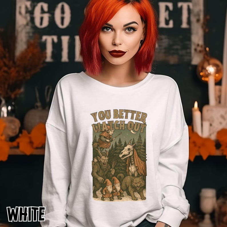 May include: White long-sleeve sweatshirt with a graphic that reads "YOU BETTER WATCH OUT." The graphic features a forest scene with various mythical creatures. The word "WHITE" is printed at the bottom of the sweatshirt.