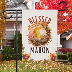 May include: A white garden flag with a brown tree and a crescent moon in the center. The text "Blessed Mabon" is printed in black letters on the flag.