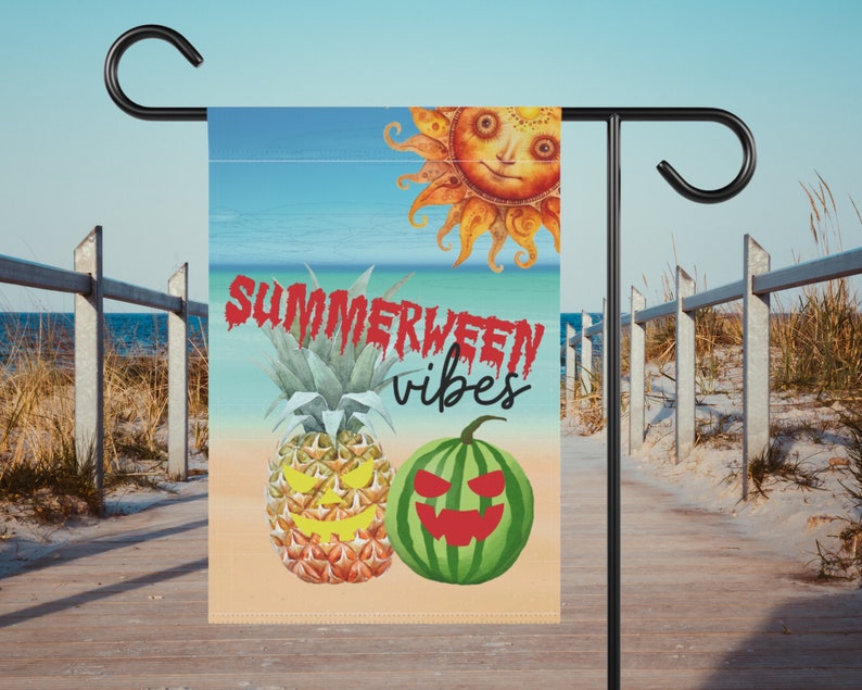 May include: A summer-themed garden flag with a bright blue sky, a yellow sun with a face, and a beach scene. The text "SUMMERWEEN vibes" is written in red dripping letters. A pineapple and a watermelon with jack-o-lantern faces are in the foreground.