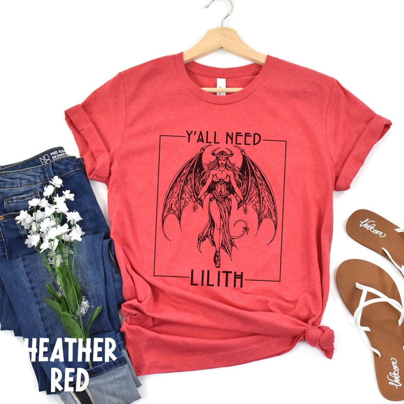 Puede incluir: Camiseta roja de mezcla con un gr&aacute;fico en blanco y negro de una mujer con alas y cola. El texto "Y'all Need Lilith" est&aacute; impreso en la camiseta.