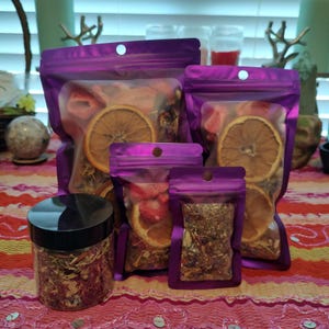 May include: Assortment of dried fruit and herbs in clear and purple packaging. The image features a clear jar with a black lid, and several purple zip-lock bags of varying sizes. The bags contain dried orange slices, strawberries, and herbs.
