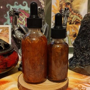 Peut inclure: Deux flacons en verre ambr&eacute; avec des compte-gouttes remplis d'un liquide dor&eacute; contenant de petites particules brillantes. Les flacons sont pos&eacute;s sur une surface en bois.