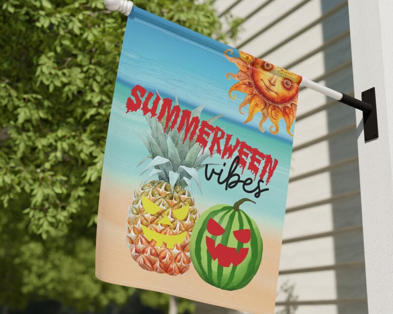 May include: A summer-themed garden flag with a beach scene, a pineapple, a watermelon, and a sun with a smiling face. The text on the flag reads "Summerween vibes".