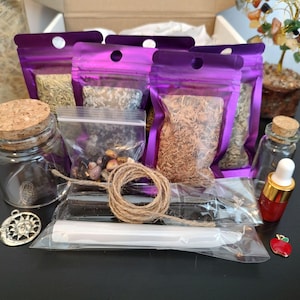 May include: A collection of spiritual items, including purple pouches filled with herbs, small glass jars with cork stoppers, a small glass bottle with a dropper, a bundle of twine, and a silver charm. The items are arranged in a box.