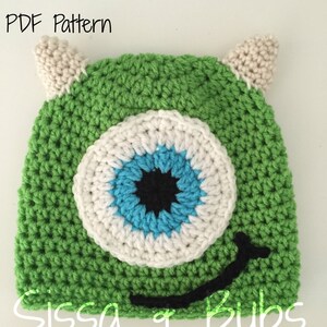 May include: Green crocheted hat with a large blue eye, white and black accents, and a black smiling mouth. The hat has two white horns on top. The text "PDF Pattern" is at the top of the image and "Sissa & Bubs" is at the bottom.