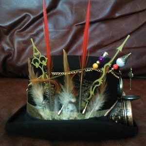 May include: A black top hat with a gold chain, feathers, and beads. The hat has a pocket watch and a key attached to it.