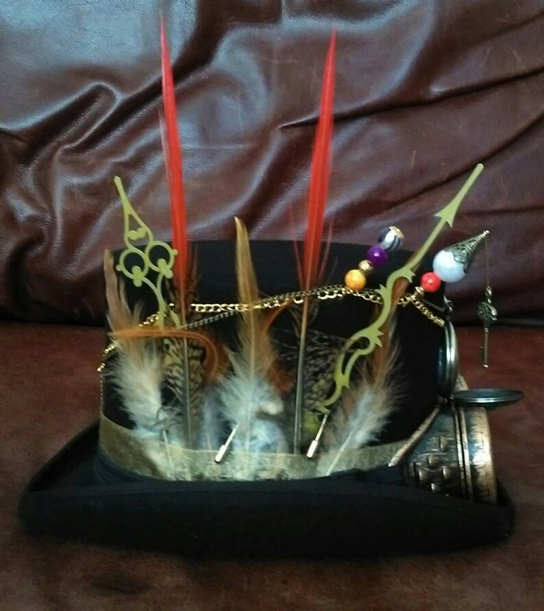 May include: A black top hat with a gold chain, feathers, and beads. The hat has a pocket watch and a key attached to it.