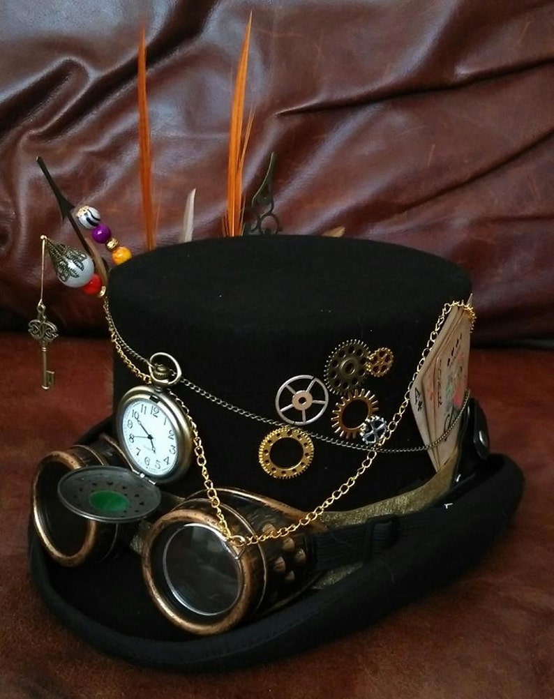 May include: A black top hat with a variety of steampunk embellishments, including gears, a pocket watch, goggles, and playing cards. The hat is decorated with feathers and beads.