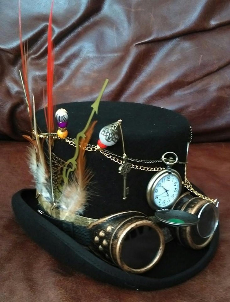 May include: A black top hat with a gold chain, a pocket watch, and goggles. The hat is decorated with feathers and beads.