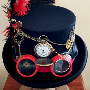 May include: A black top hat with red and black feathers, a pocket watch, and goggles. The hat is decorated with gears and chains.