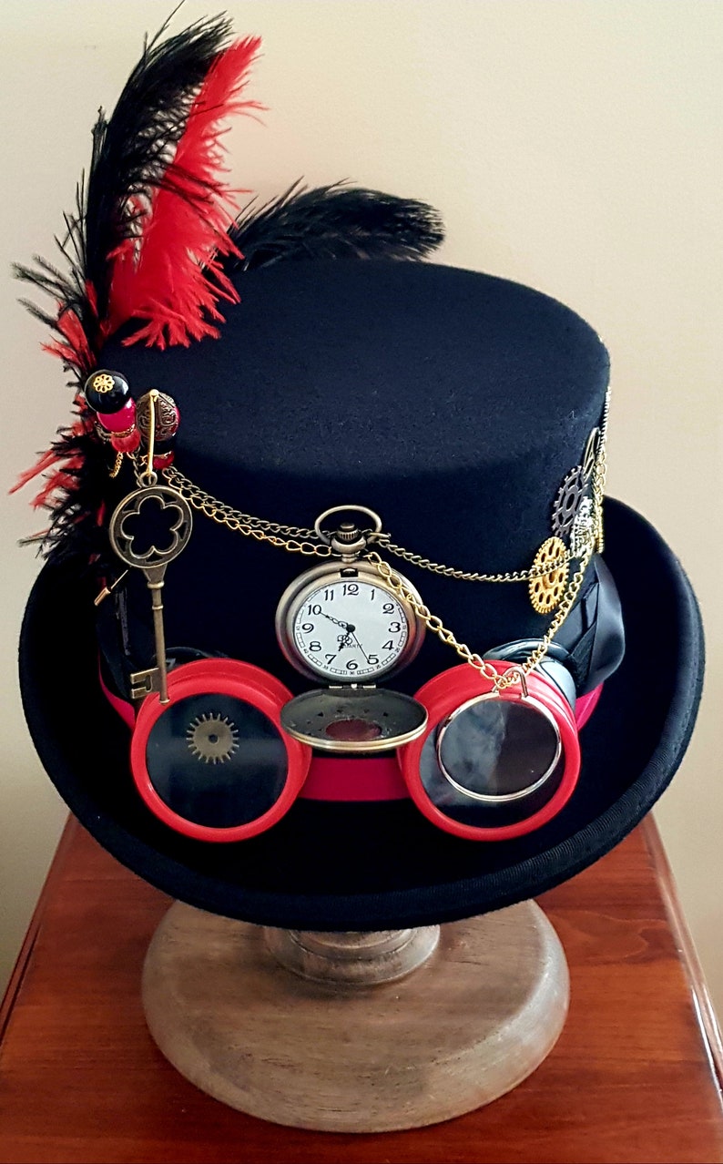 May include: A black top hat with red and black feathers, a pocket watch, and goggles. The hat is decorated with gears and chains.