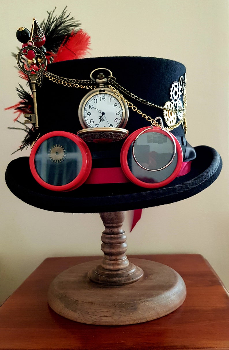 May include: A black top hat with a red ribbon, gold chain, and a pocket watch. The hat also has goggles with red frames and a key with red beads attached to it.