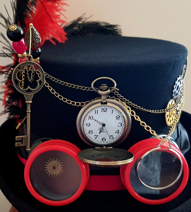 May include: A black top hat with a red and black feather, a gold chain, a pocket watch, and red goggles with a brass gear detail.