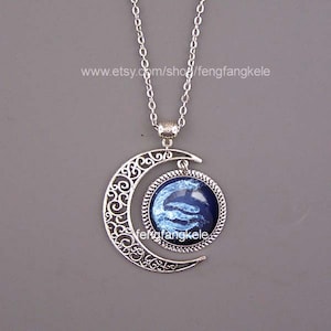May include: Silver necklace with a crescent moon pendant and a round glass charm featuring a blue and white swirling design. The charm is set in a silver frame.