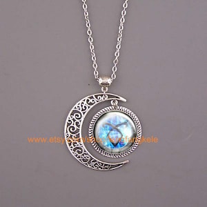May include: A silver necklace with a crescent moon pendant featuring a blue and black glass cabochon with a symbol inside. The symbol is a stylized rune or glyph.