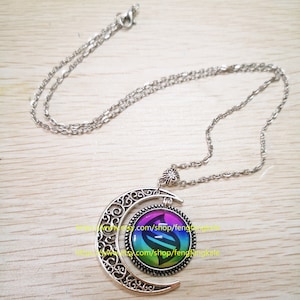 Op de afbeelding: Een zilveren halve maan ketting met een regenboogkleurige glazen hanger met een gestileerd 'S'-symbool. De hanger is gezet in een zilveren bezel.