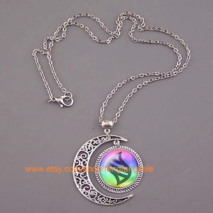 Op de afbeelding: Een zilveren ketting met een halve maan hanger. De hanger heeft een ronde, regenboogkleurige glazen cameo met een zwart-wit DNA-symbool erin. De tekst "www.etsy.com/shop/fengfangle" is zichtbaar op de cameo.