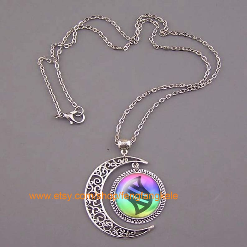 Op de afbeelding: Een zilveren ketting met een halve maan hanger. De hanger heeft een ronde, regenboogkleurige glazen cameo met een zwart-wit DNA-symbool erin. De tekst "www.etsy.com/shop/fengfangle" is zichtbaar op de cameo.