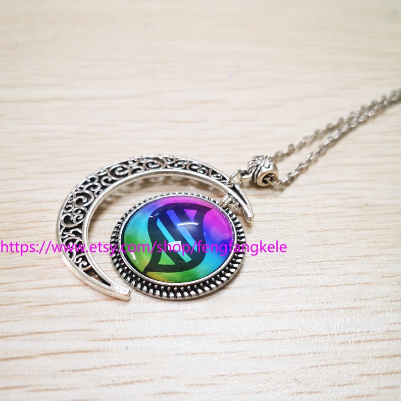 Op de afbeelding: Een zilveren halve maan ketting met een regenboogkleurige glazen hanger met een DNA-symbool. De hanger is omgeven door een zilveren rand.