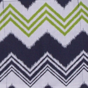 May include: A white fabric with a chevron pattern in shades of green, black, and white. The fabric has a slightly textured surface.