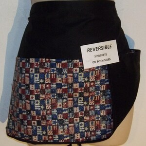 May include: Black reversible apron with a red, white, and blue patterned fabric featuring small American flags. The apron has three pockets on both sides. The text "REVERSIBLE 3 POCKETS ON BOTH SIDES" is printed on a white tag.