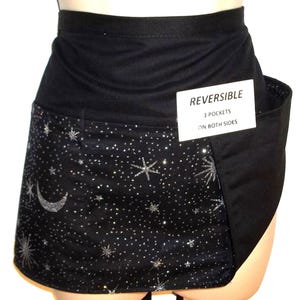 May include: Reversible black skirt with three pockets on both sides. One side features a starry night design with a crescent moon and sparkling stars. The other side is solid black. The tag reads "Reversible, 3 pockets on both sides."