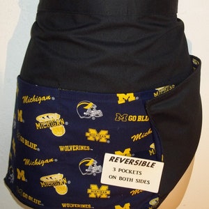 May include: Reversible black and blue apron with a Michigan Wolverines theme. The apron has three pockets on each side and features the team logo, mascot, and the phrase "Go Blue".