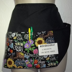 May include: Black reversible apron with three pockets on each side. The apron has a floral print with sunflowers, butterflies, and the text "You can grow your own way" and "I've got sunshine on a cloudy day".