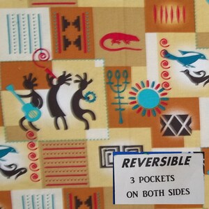 May include: A beige fabric with a colorful geometric pattern. The pattern includes stylized figures, birds, and a sun. The fabric has the text "REVERSIBLE", "3 POCKETS", and "ON BOTH SIDES" printed on a white tag.