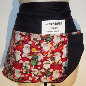 May include: A black and red reversible apron with a Santa Claus print. The apron has three pockets on both sides. The text "REVERSIBLE 3 POCKETS ON BOTH SIDES" is printed on a white tag.