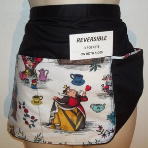 May include: A reversible black and white apron with a Mad Hatter and Queen of Hearts tea party design. The apron has three pockets on both sides. The text on the tag reads "REVERSIBLE 3 POCKETS ON BOTH SIDES".