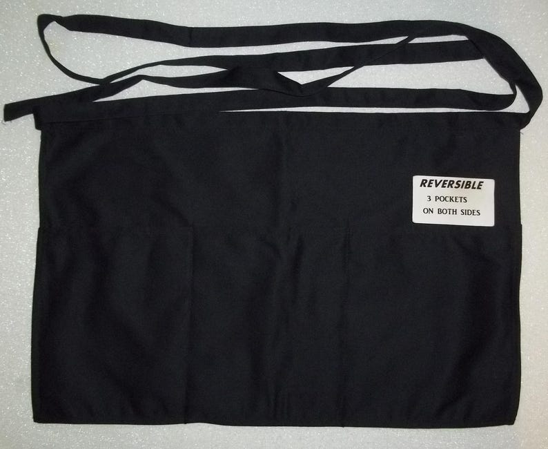 May include: Black reversible apron with three pockets on each side. The apron has a label that reads "REVERSIBLE 3 POCKETS ON BOTH SIDES".