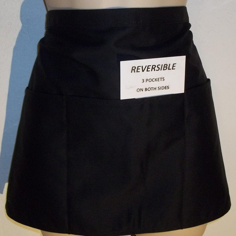 May include: Black reversible apron with three pockets on both sides. The apron has a label that reads "REVERSIBLE 3 POCKETS ON BOTH SIDES".
